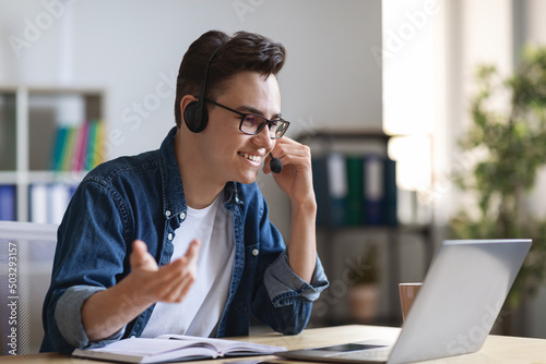 Video Call. Young Guy In Headset Making Teleconference Via Laptop In Office