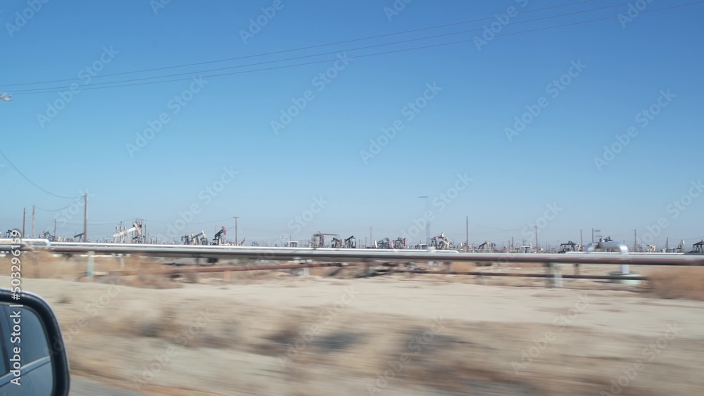 Wells with pump jacks on oil field, California USA. Rigs for crude fossil extraction working on oilfield. Industrial landscape, derricks in desert valley. Many pumpjacks platforms on oilwells pumping.