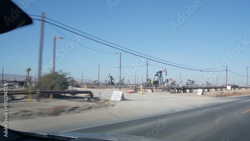 Wells with pump jacks on oil field, California USA. Rigs for crude fossil extraction working on oilfield. Industrial landscape, derricks in desert valley. Many pumpjacks platforms on oilwells pumping. © Dogora Sun