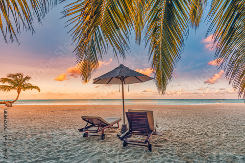 Beautiful tropical sunset landscape, couple sun beds, loungers, umbrella under palm tree. White sand, seaside horizon, colorful twilight sky, calm and relax, recreational. Inspirational beach resort 