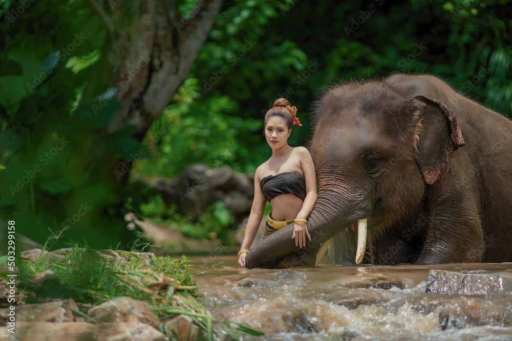 Fototapeta premium Portrait of a woman standing in a river with an elephant, Thailand.