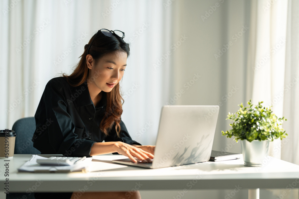 Asian young woman in smart casual wear working on laptop and calculator while sitting in creative office. Asian young woman in smart casual wear working on laptop and calculator while sitting in creative office.