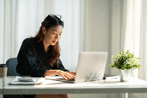 Obraz na plátně Asian young woman in smart casual wear working on laptop and calculator while sitting in creative office