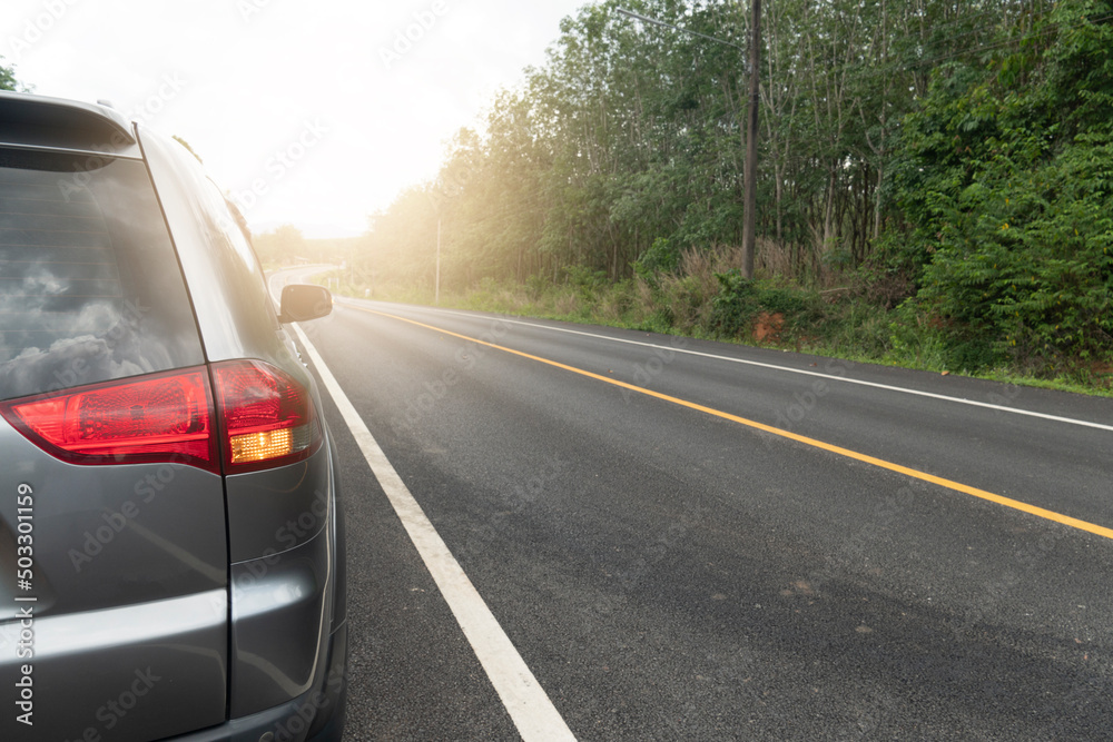 Car running on the asphalt road for travel trip a straight curved path forward. With green forest beside road. Tail lamp of car turn on light signl. White line and the solid yellow line on the road. Car running on the asphalt road for travel trip a straight curved path forward. With green forest beside road. Tail lamp of car turn on light signl. White line and the solid yellow line on the road.