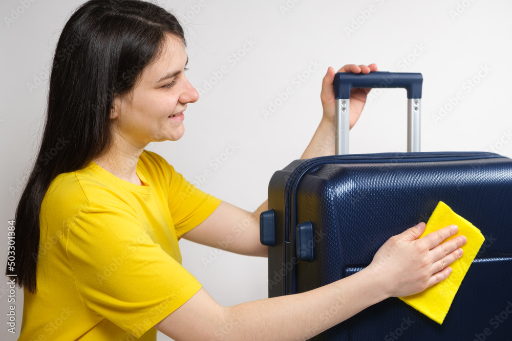 A woman wipes a travel plastic blue suitcase with a yellow rag. Care of the suitcase, removal of scratches and dust. A woman wipes a travel plastic blue suitcase with a yellow rag. Care of the suitcase, removal of scratches and dust.