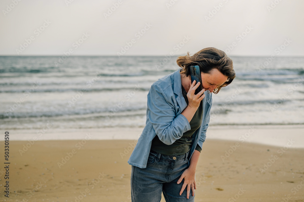 a young woman on the beach near the ocean in the spring at sunset talking on the phone with a smile on her face to her loved ones, friends to share the joy of vacation. modern technologies