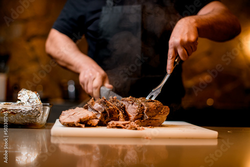 Man cuts hot fried meat to slices on cutting board.