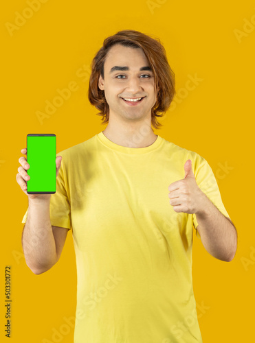 Young man Prep Student with long hair. 20s guy with smartphone on a yellow background