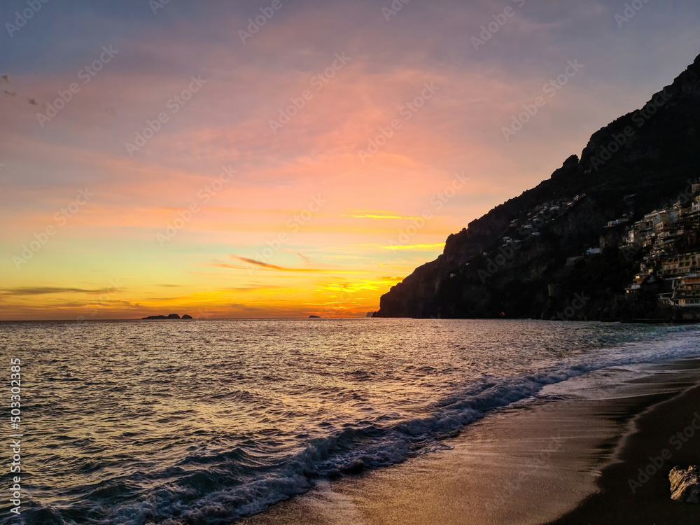 Fototapeta premium Panoramic sunset view on Marina Grande Beach and colorful buildings of hillside village Positano at Amalfi Coast, Italy, Campania, Europe. Ocean waves Tyrrhenian, Mediterranean Sea. Coastline