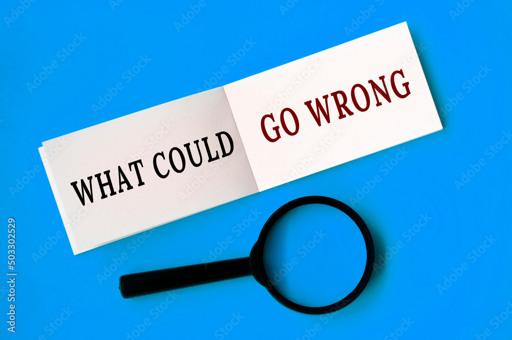 What could go wrong text on notepad with magnifying glass on blue background. Conceptual