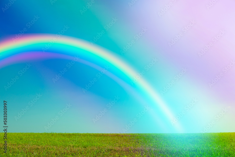 Picturesque view of green meadow and beautiful rainbow in blue sky on sunny day Picturesque view of green meadow and beautiful rainbow in blue sky on sunny day