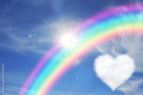 Beautiful view of heart shaped cloud, rainbow and sun in blue sky © New Africa