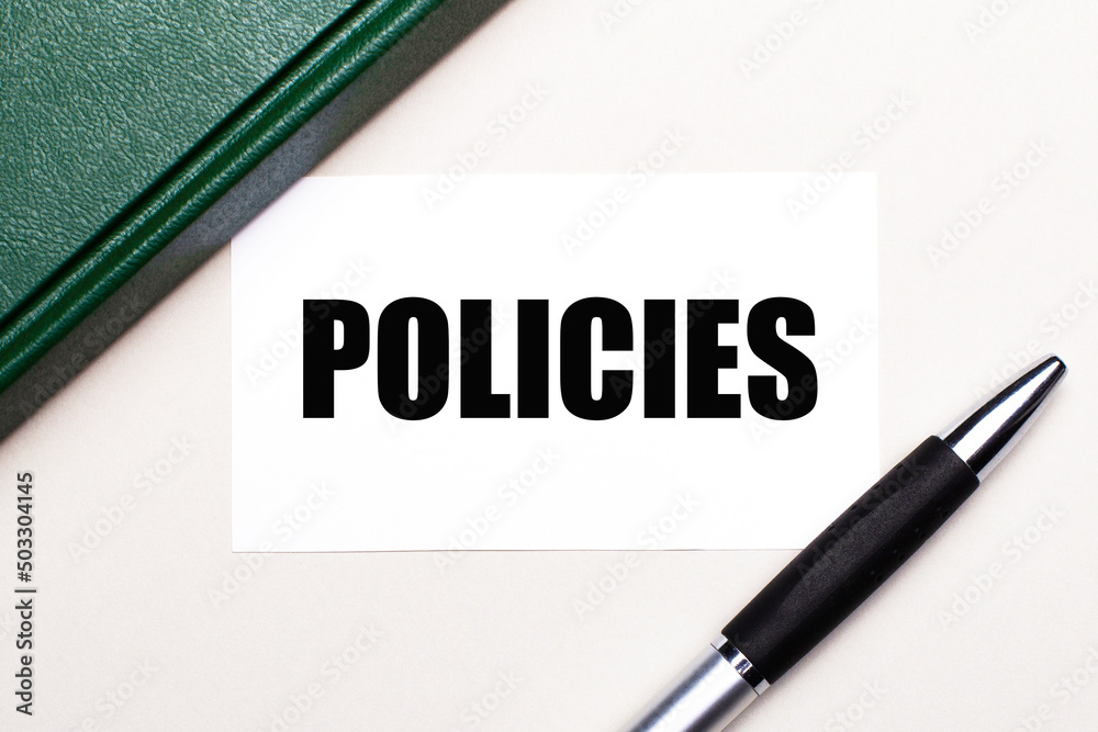 On a light gray background lies a pen, a green notebook and a white card with the text POLICIES. Business concept. On a light gray background lies a pen, a green notebook and a white card with the text POLICIES. Business concept.