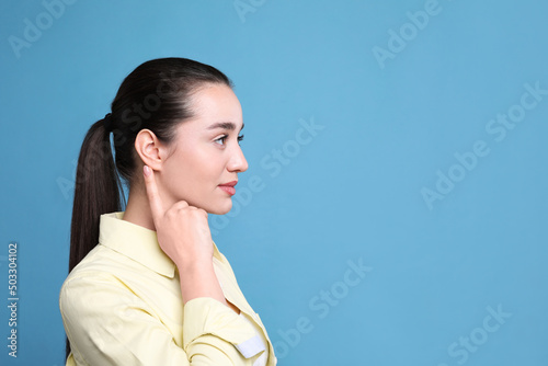 Young woman pointing at her ear on light blue background. Space for text photo