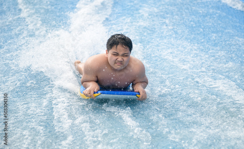 Obese Boy play wave machine on surfboard, recreation and sport © kwanchaichaiudom