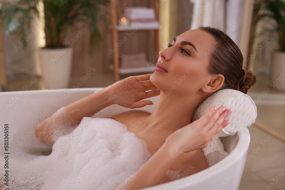 Young woman using pillow while enjoying bubble bath indoors Young woman using pillow while enjoying bubble bath indoors