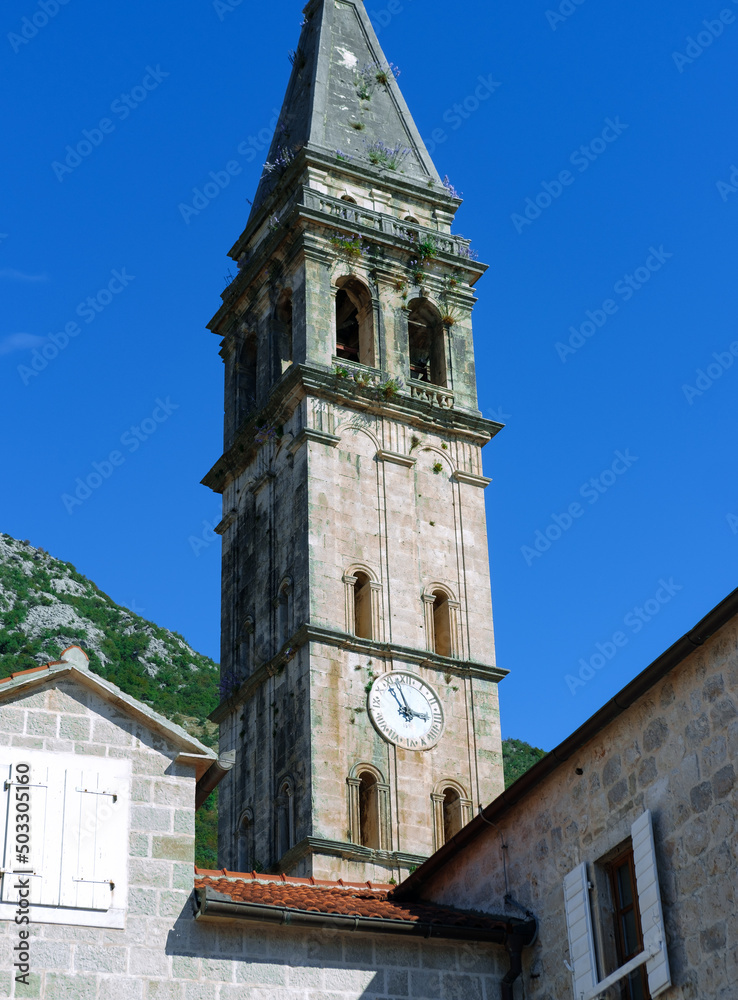 Perast town, Montenegro - 16 october 2021 : Clock tower in Perast sailor and fisherman village or town on Adriatic coast, blue sky, stone ancient architecture, middleage cultural heritage