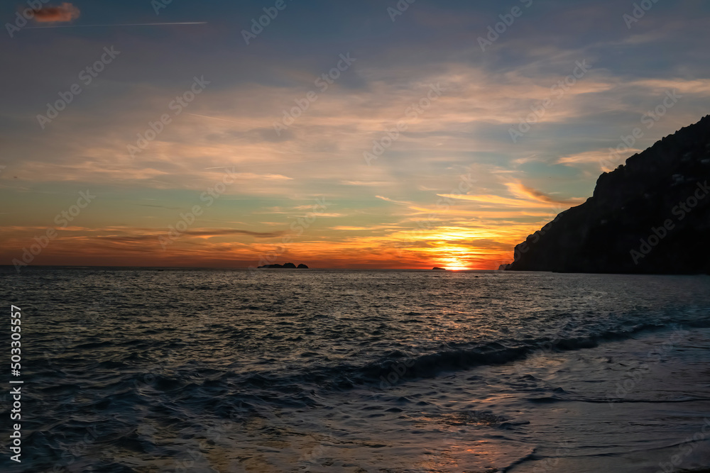 Panoramic sunset view from Marina Grande beach in Positano at Amalfi Coast, Italy, Campania, Europe. Silhouette of boat. Orange twilight over Li Galli islands in Mediterranean Sea. Reflection