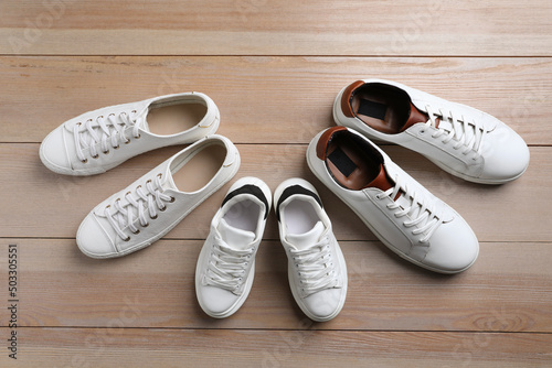 Set of new stylish white sneakers for entire family on wooden background, flat lay