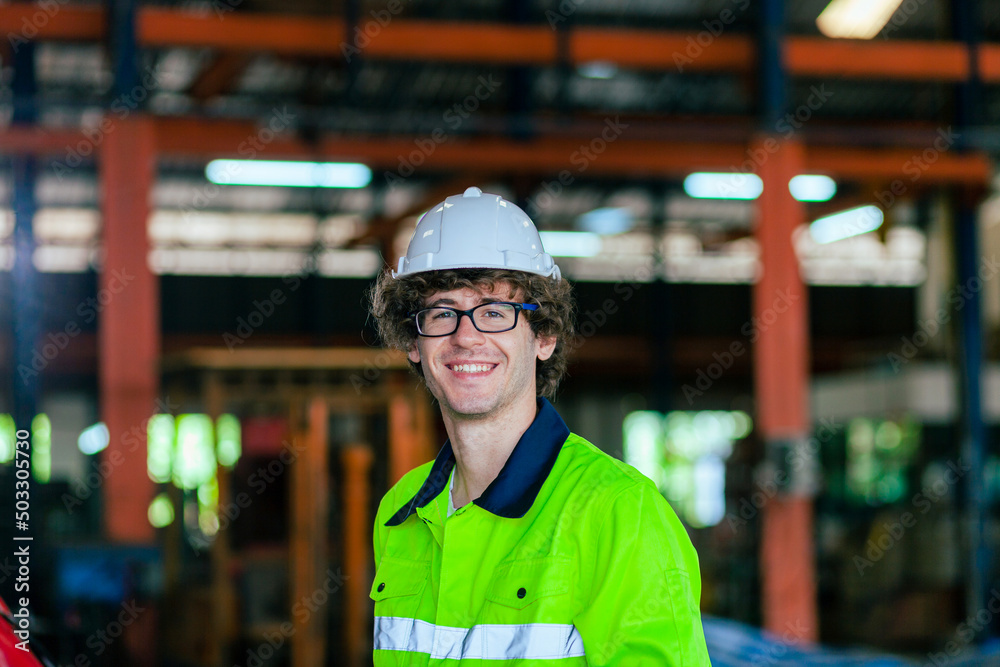 Happy professional workers wearing safety vests and hard hats in a large warehouse in the background with machines in an industrial factory.
