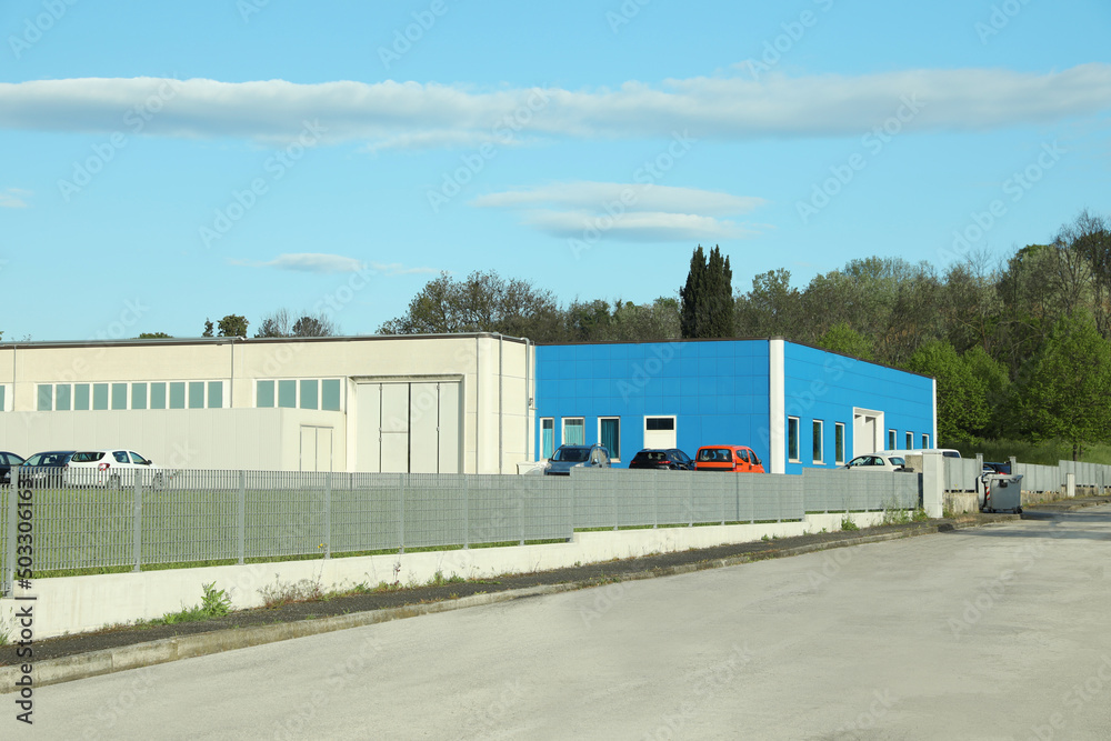 Factory building with parking lot surrounded by fence on sunny day Factory building with parking lot surrounded by fence on sunny day