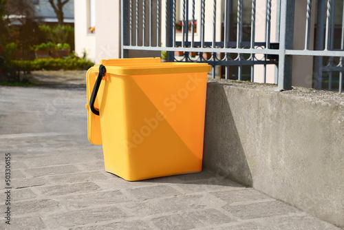 Yellow trash bin near fence outdoors on sunny day © New Africa
