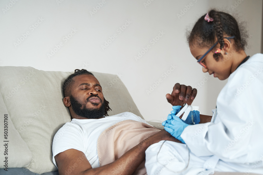 Fototapeta premium African American girl in medical gown measures the indicators of a lying father