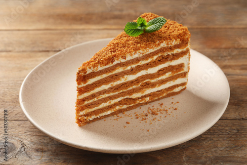 Slice of delicious layered honey cake with mint on wooden table