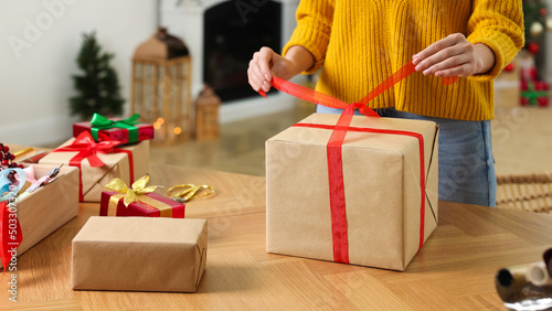Woman wrapping Christmas gift at wooden table indoors, closeup