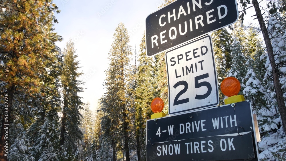 Chains or snow tires required traffic sign, mountains winter highway, Yosemite snowy forest, California USA. Icy road caution or warning, safety during snowfalls for transport. Speed limit in woods