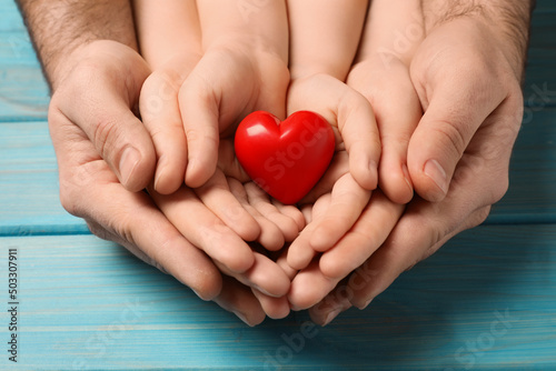 Parents and kid holding red heart in hands at light blue wooden table  closeup