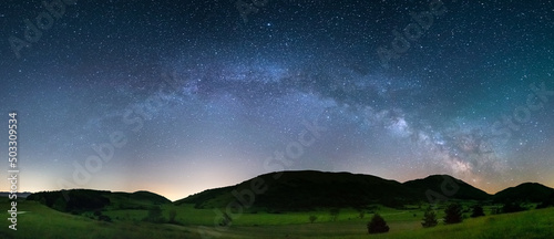 Panoramic night sky over Montelago highlands, Marche, Italy. The Milky Way galaxy arc and stars in unique hills landscape.