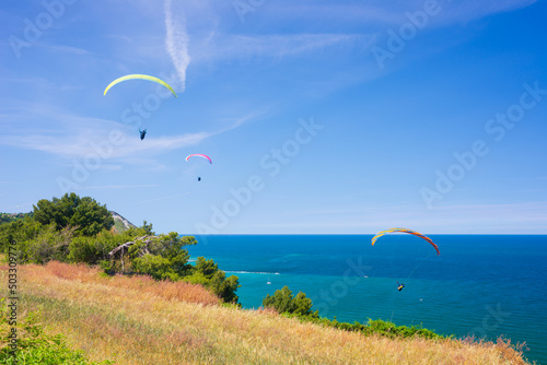 Paragliders flying over scenic coast line of the Conero natural, Italy. Extreme sport over dramatic coast headland in the mediterranean sea tourism destination