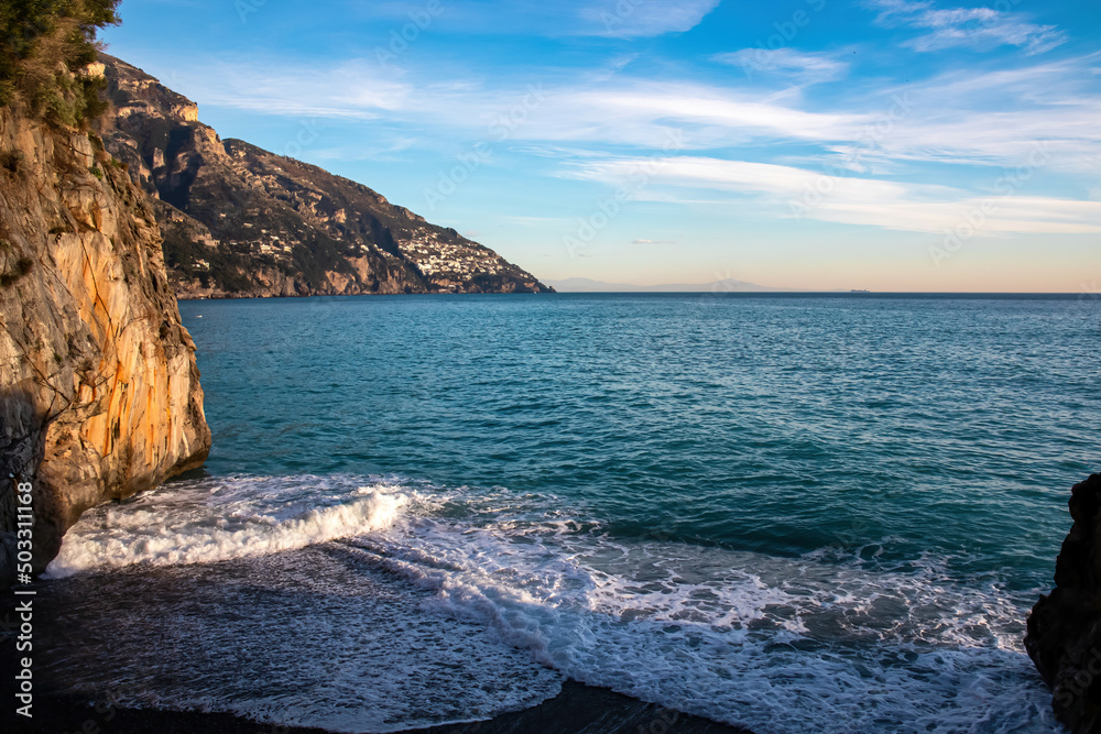 Rock formation with panoramic view at Fornillo Beach in coastal town Positano, Amalfi Coast, Italy, Campania, Europe. Vacation at the coastline of Mediterranean Sea. Village of Praiano in distance.