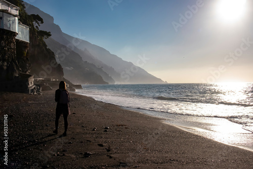 Woman walking during sunrise at marina grande Beach in town Positano  Amalfi Coast  Italy  Campania  Europe. Luxury vacation Tyrrhenian  Mediterranean Sea. Early morning sunbeam reflection in sand