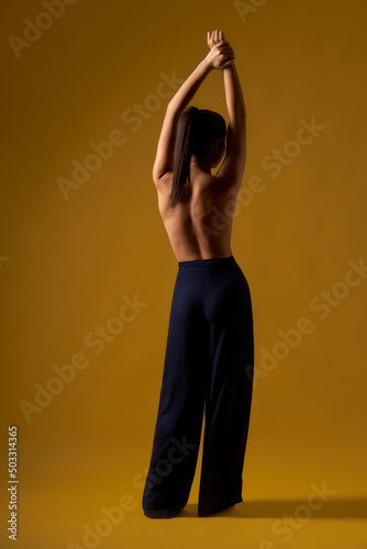 Back view of female with pony tail doing yoga indoors. Flexible woman with bare back standing backwards, raising hands, meditating. Concpt oof yoga doing 