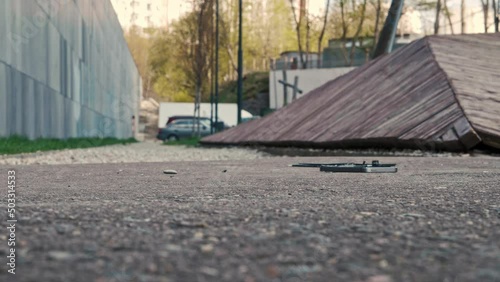 A small silver mobile phone falls from a height to the asphalt, breaks in slow motion and shatters into pieces on the ground. A sunny summer day in the parking lot of a residential building. Close up.