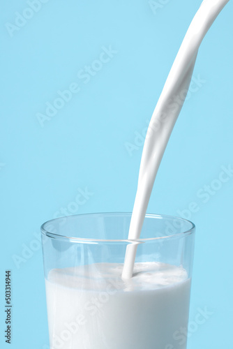 On a blue background fresh milk is pouring into the glass close up