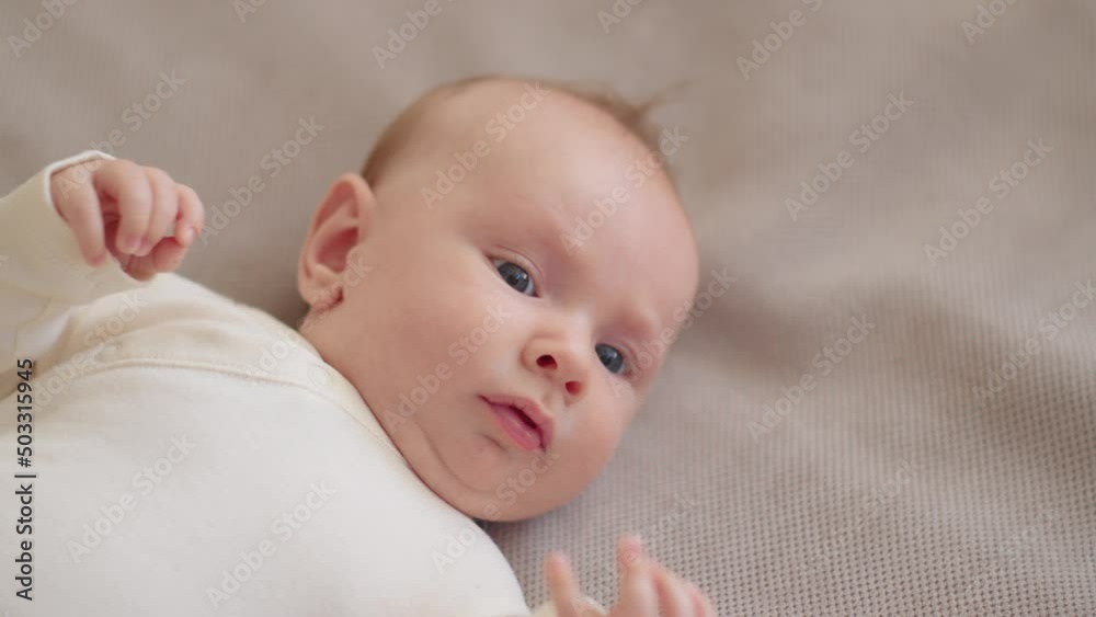 Happy two-month-old baby in blue clothes looks into camera, slow motion. Active and cheerful newborn boy lies on the sofa and moves his arms. Funny and cute chubby male baby. Beautiful infant. Happy two-month-old baby in blue clothes looks into camera, slow motion. Active and cheerful newborn boy lies on the sofa and moves his arms. Funny and cute chubby male baby. Beautiful infant.