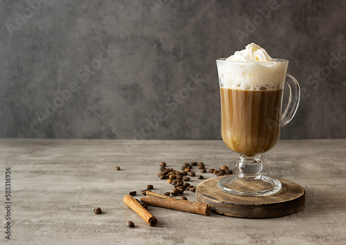 Black coffee with air cream on a dark brown wooden stand. Coffee beans and cinnamon straws on the table. Dark gray background, space for text