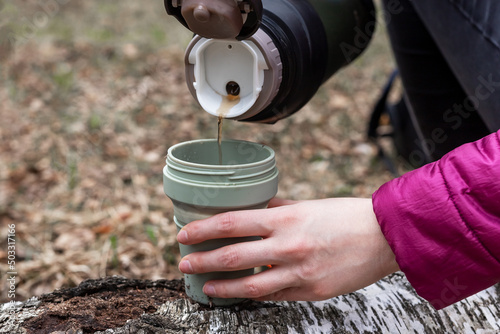 Woman hands pouring tea from thermos into cup. Hot drink break during hiking or camping in autumn or spring time. High quality photo