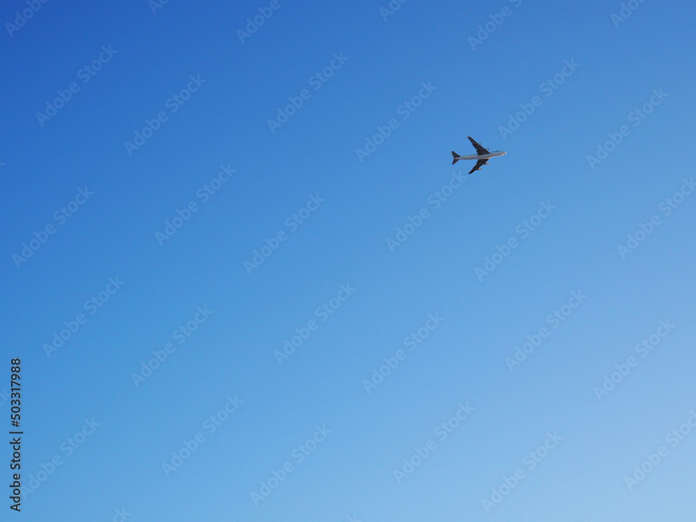 The big four-engine transport airplane is flying far away. Clear blue sky. International air freight. Background or backdrop