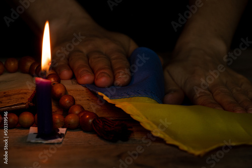 Women's hands hold the flag of Ukraine and pray near the candle for the country in the dark, stop the war in Ukraine