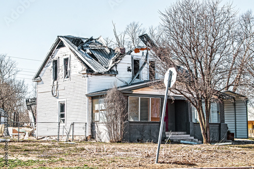 Two story frame house that has been hit by a tornado with roof caved in and debris hanging out of second story window in rural Oklahoma USA