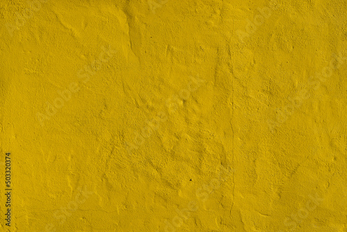 Yellow painted wall background texture. Uneven surface of a building exterior. Vintage backdrop for the use as copy space. Grungy structure of an old house.