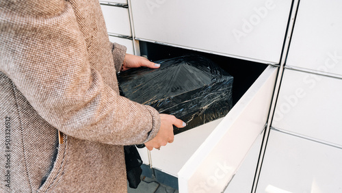 Pickup parcel. Courier box in woman hands at post delivery automat terminal. Self service post terminal and parcel delivery concept. photo