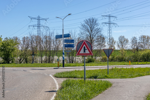 Country road with a caution triangle next crossroads and signs indicating the direction to Echt, Maastricht, Ohe en Laak, Maasbracht and Eindhoven in Stevensweert, South Limburg, Netherlands photo