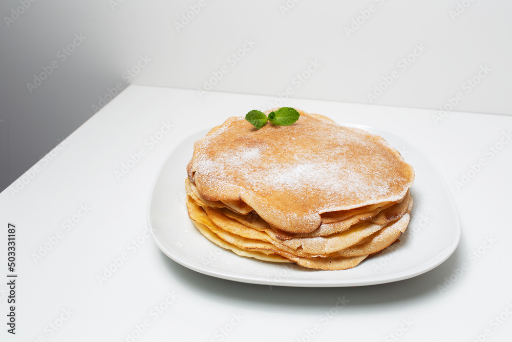 Picture of vegan thin pancakes, on the white plate, decorated with mint leaf.