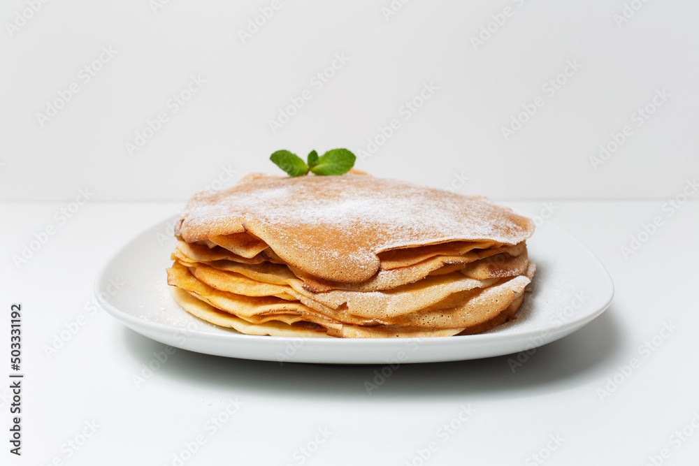 Photo of vegan thin pancakes, on the white plate, decorated with mint leaf. Photo of vegan thin pancakes, on the white plate, decorated with mint leaf.