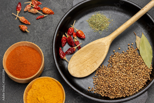 Wooden spoon, coriander seeds and pepper pods in frying pan photo